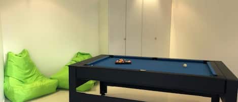A pool table with balls, green bean bag chairs, and a cabinet.