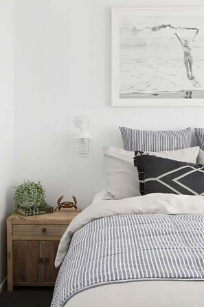 Ein Schlafzimmer mit Bett, Kissen, einem Nachttisch, einer Wandlampe und einem gerahmten Bild.