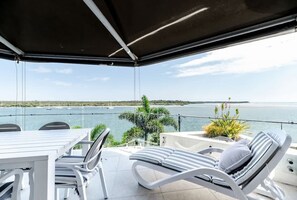 Un espace extérieur aménagé, abrité et doté d’une vue sur la mer, avec une table, des chaises et un fauteuil.