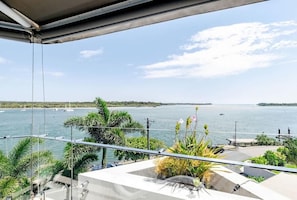 Ein Balkon mit Blick auf ruhiges Wasser, Palmen und eine entfernte Küste.