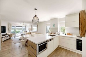 Une cuisine moderne dotée d’un îlot central, de meubles blancs et d’une grande fenêtre offrant une vue dégagée.