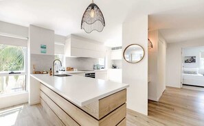 Une cuisine moderne dotée d’un grand îlot central, de meubles blancs et d’un luminaire suspendu.