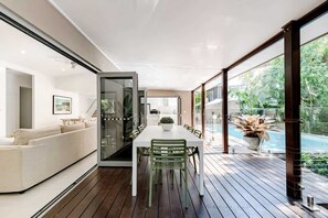 A modern interior with a dining area, a sofa, and a view of a swimming pool. - Sleek Stylish Family Beach House Near Junction (Noosa)