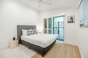 A bedroom with a bed, a ceiling fan, a window with blinds, a small plant, and a picture on the wall. - Sleek Stylish Family Beach House Near Junction (Noosa)