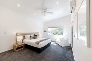 A modern bedroom with a bed, bedside tables, a ceiling fan, and a window with a view. - Sleek Stylish Family Beach House Near Junction (Noosa)