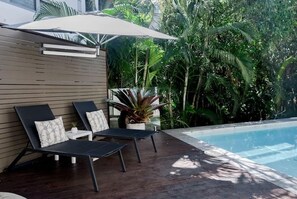 A poolside area with two lounge chairs, a large umbrella, and lush tropical vegetation. - Sleek Stylish Family Beach House Near Junction (Noosa)