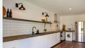 A modern kitchen with white cabinets, a wooden countertop, a built-in washing machine, and pendant lighting.