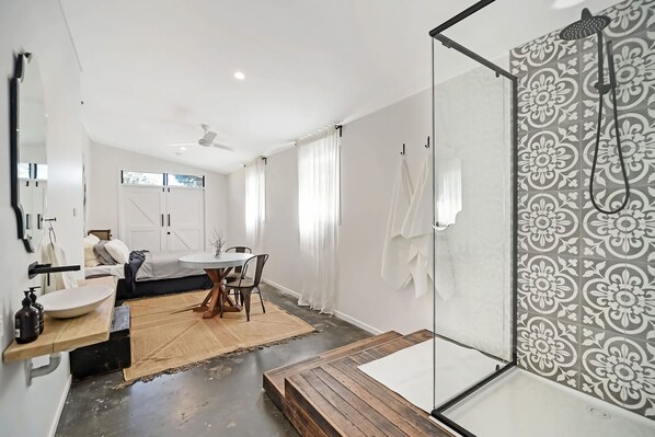 A modern bathroom with a glass shower enclosure, a wooden bench, and a large mirror.