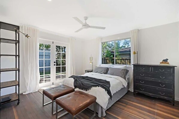 A bedroom with a bed, a bench, a dresser, a ceiling fan, and a window. - The River Shack Vintage Luxe Right Beside River (Noosa)