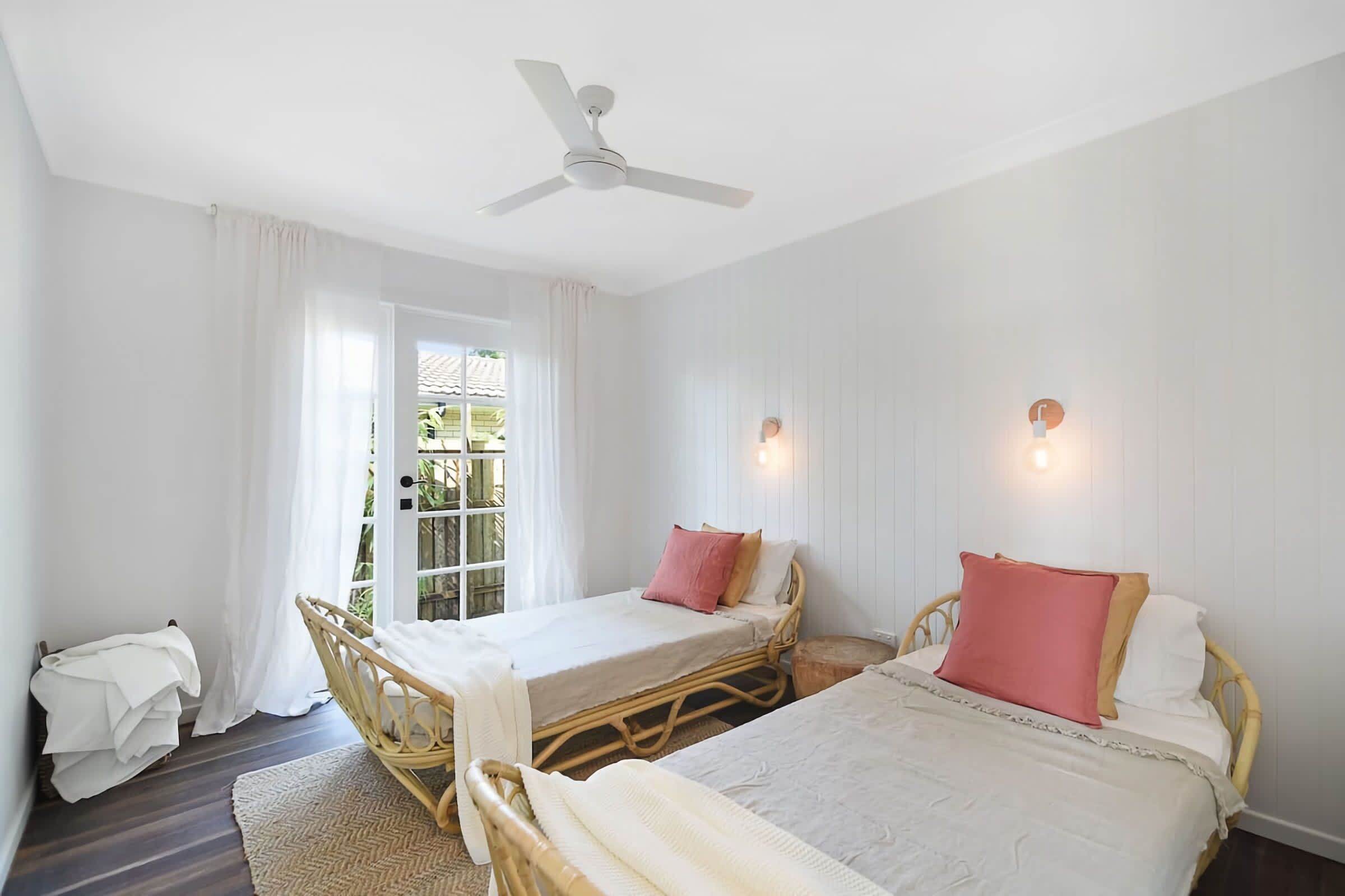 A bedroom with two beds, a ceiling fan, and a window with curtains.