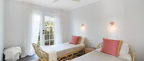 A bedroom with two beds, a ceiling fan, and a window with curtains.