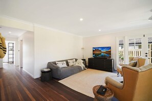 A modern living room with a grey sofa, a black entertainment unit, and a large flat-screen TV. - The River Shack Vintage Luxe Right Beside River (Noosa)
