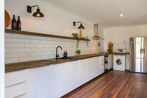 Cozinha moderna com armários brancos, bancada de madeira, máquina de lavar embutida e frigorífico de aço inoxidável.
