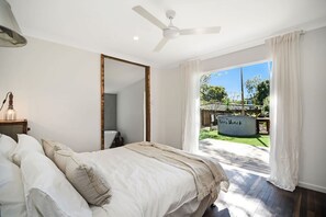 A bedroom with a bed, a ceiling fan, a large mirror, and a view of a backyard with a pool. - The River Shack Vintage Luxe Right Beside River (Noosa)