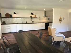A modern kitchen with white cabinets, a wooden countertop, and a dining area with a dark wooden table and metal chairs. - The River Shack Vintage Luxe Right Beside River (Noosa)