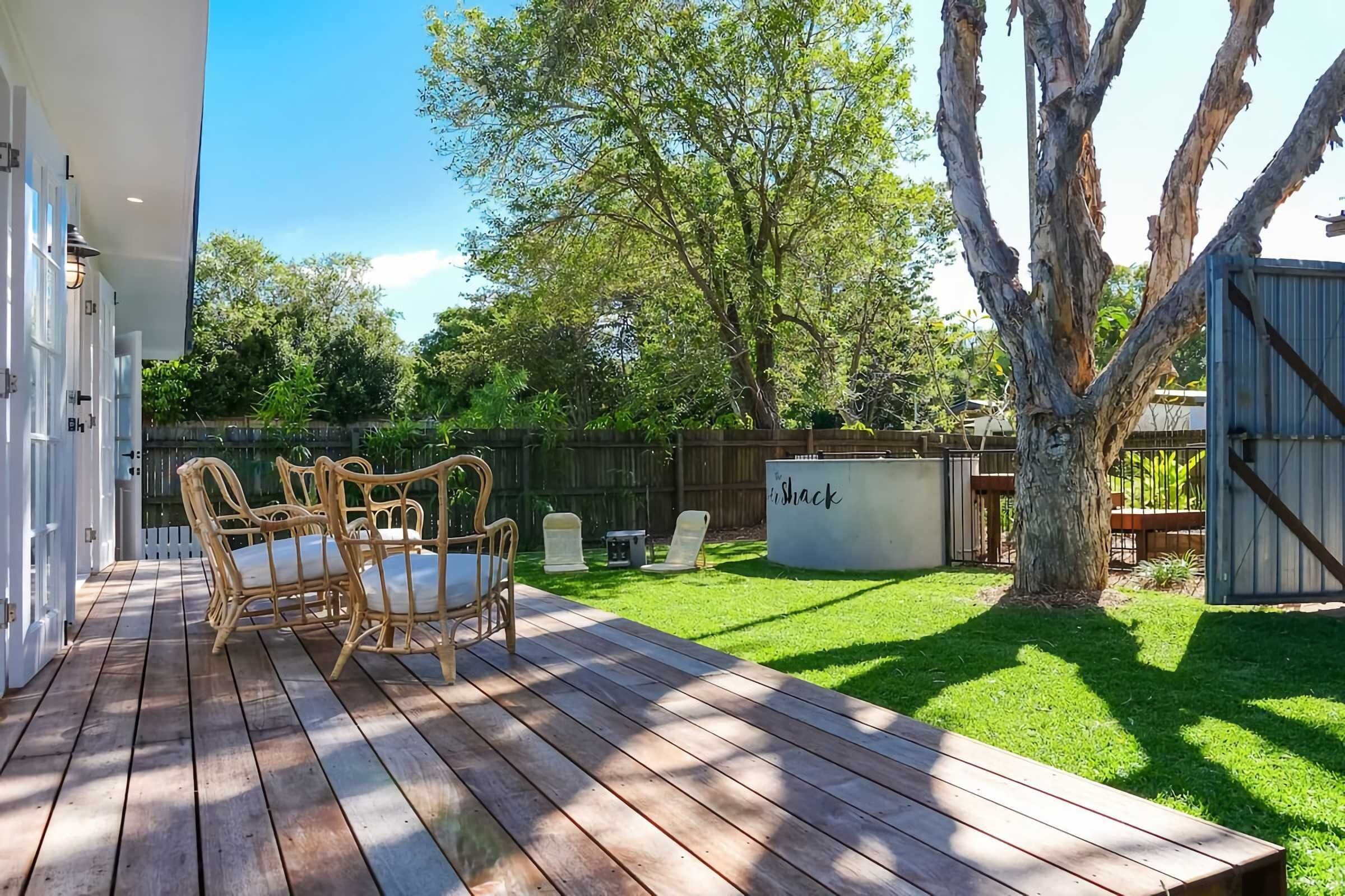Una terraza de madera con mobiliario exterior, un patio cercado y un árbol.