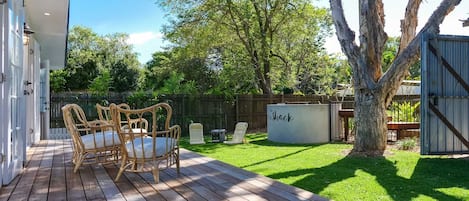 Una terraza de madera con mobiliario exterior, un patio cercado y un árbol.