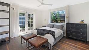 A bedroom with a bed, a bench, a dresser, a ceiling fan, and a window.