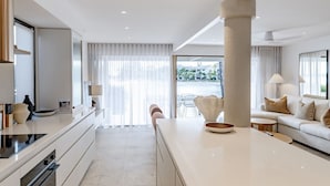 Een moderne keuken met een centraal eiland, een zithoek met een bank, en uitzicht door grote ramen.