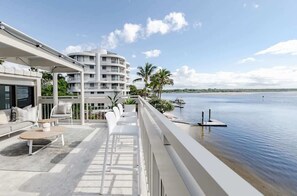 Een balkon met zitgelegenheid buiten, uitzicht op het water en een gebouw met meerdere balkons.