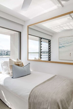 A modern bedroom with a large bed, a window with blinds, a mirror, and a painting on the wall. - Bella Vista Noosa Luxury on White Sands (Noosa)