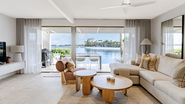 Een moderne woonkamer met een groot raam, een plafondventilator en uitzicht op een waterpartij.