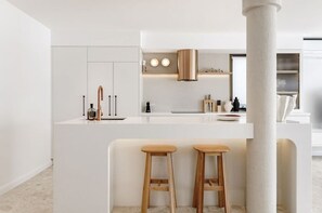Een moderne keuken met witte kasten, een centraal eiland met krukken en een grote kolom.