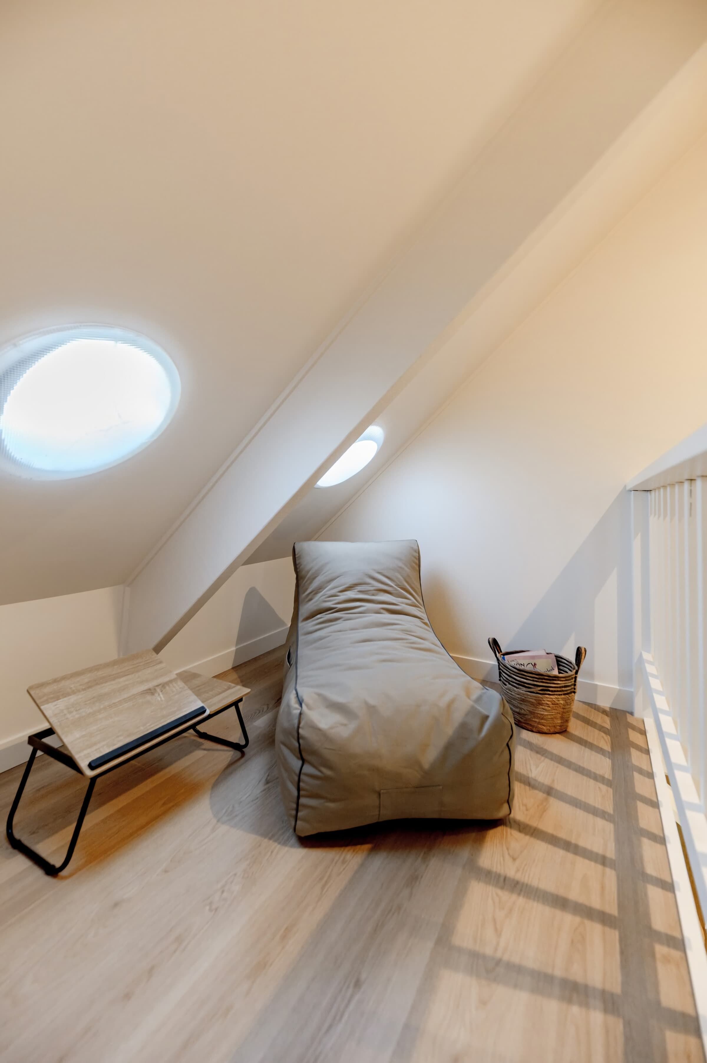 Une petite pièce avec un plafond en pente, comprenant un lit, une table et un panier.
