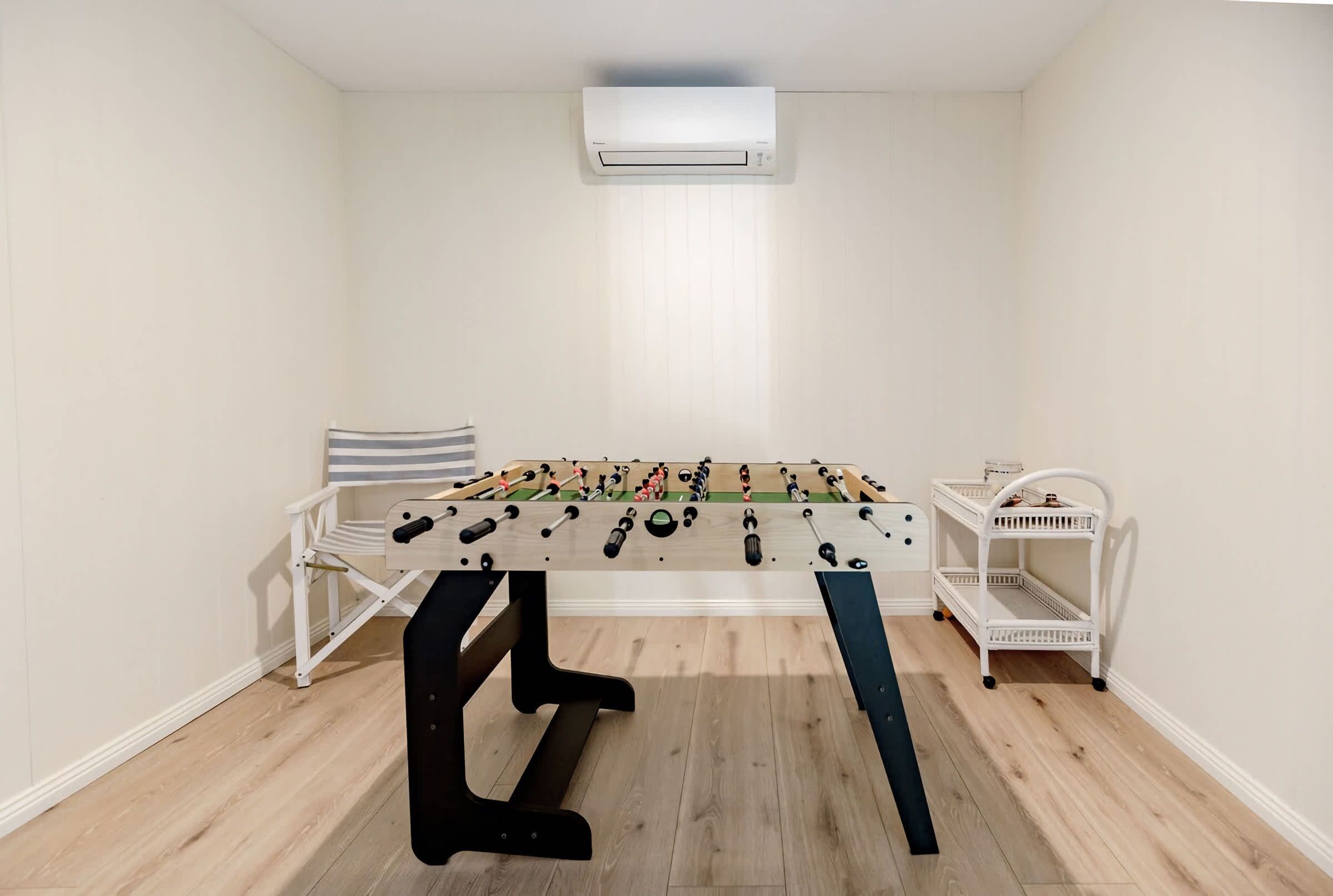 Une pièce avec une table de baby-foot, une étagère blanche et un climatiseur.