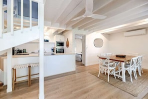 A modern kitchen with white cabinetry, a dining area with white chairs, and a staircase. - The Rest Family Cottage with Resort Style Pool (Noosa)