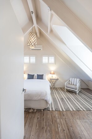 A bedroom with a sloped ceiling, a bed, a chair, and a patterned rug.