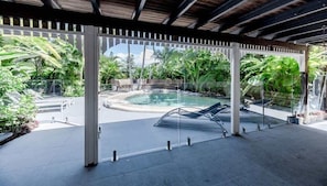 A covered outdoor swimming pool with lounge chairs, surrounded by tropical plants. - The Rest Family Cottage with Resort Style Pool (Noosa)
