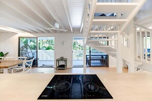 A modern kitchen with a central island, white wooden beams, and a staircase leading to an upper level.