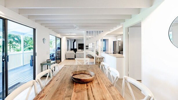 Un intérieur moderne avec une table à manger en bois, des chaises blanches, un coin cuisine et un balcon offrant une vue.