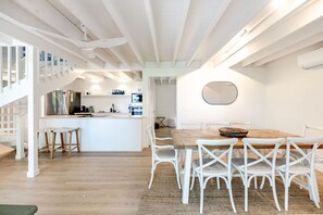 A modern kitchen with white cabinetry, a central island, and a dining area with white chairs and a wooden table.