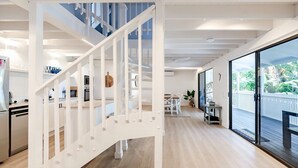 Un intérieur moderne comprenant un escalier, une cuisine, un coin repas et de grandes portes-fenêtres coulissantes donnant sur une terrasse extérieure.