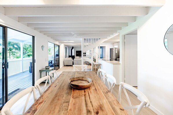 A modern interior with a wooden dining table, white chairs, and a view of the outdoors through large windows.