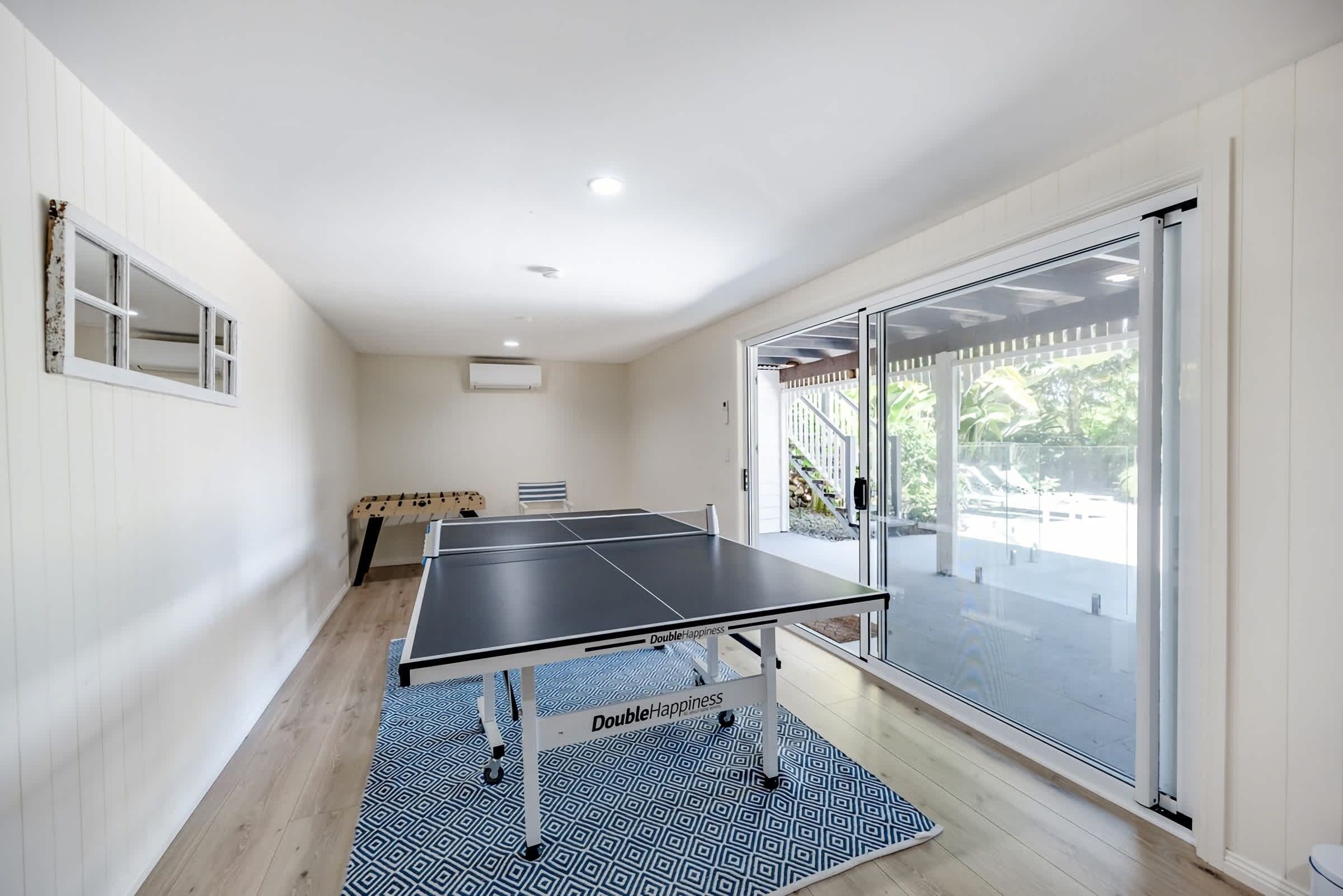 Une pièce avec une table de ping-pong, un canapé et une grande porte vitrée donnant sur l’extérieur.