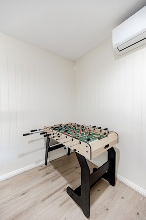 A room with a foosball table, white walls, and a ceiling-mounted air conditioning unit. - The Rest Family Cottage with Resort Style Pool (Noosa)