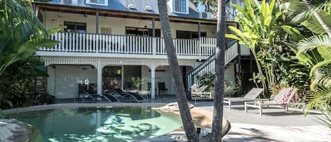 A two-story building with a pool, outdoor seating, and tropical vegetation.