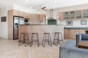 A modern kitchen with a central island, bar stools, a ceiling fan, and light-colored cabinetry.