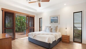 A bedroom with a bed, a nightstand, a ceiling fan, and a large window with blinds. - Seahorse Family & Pooch Friendly Waterfront Home (Noosa)
