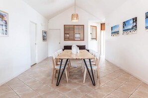 A dining area with a wooden table and chairs, a hanging light fixture, and a window with blinds. - Seahorse Family & Pooch Friendly Waterfront Home (Noosa)