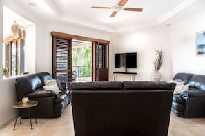 Un salon avec deux canapés en cuir noir, un ventilateur de plafond, un téléviseur et une vue sur l’extérieur.