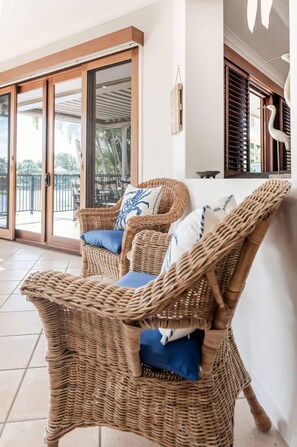 A wicker chair with cushions, a sliding glass door, and a white wall with a decorative bird sculpture. - Seahorse Family & Pooch Friendly Waterfront Home (Noosa)
