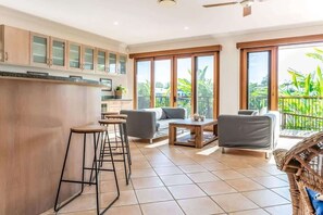 A modern kitchen with a bar area, a dining space with a sofa and coffee table, and large sliding glass doors to a balcony. - Seahorse Family & Pooch Friendly Waterfront Home (Noosa)