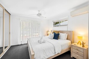 A bedroom with a bed, bedside table, lamp, and a window with blinds.