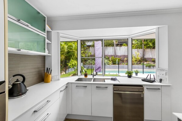 Una cocina moderna con muebles blancos, una tetera y un escurreplatos.