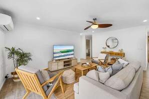 Ein modernes Wohnzimmer mit Fernseher, Deckenventilator, Sofa, Couchtisch und einem Beistelltisch mit Dekoration.