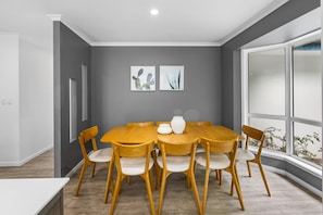 Un espace repas avec une table et des chaises en bois, des murs gris et deux œuvres d’art encadrées.